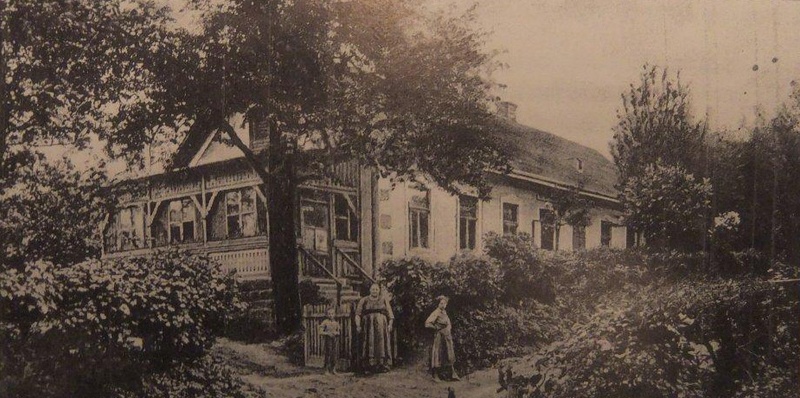 Altes schwarz-weiß Foto des Kaufhauses Straßhofer aus den 1930er Jahren. Im Vordergrund steht eine Frau mit zwei Kindern an einem Holzzaun, im Hintergrund ist das Geschäft zu sehen.